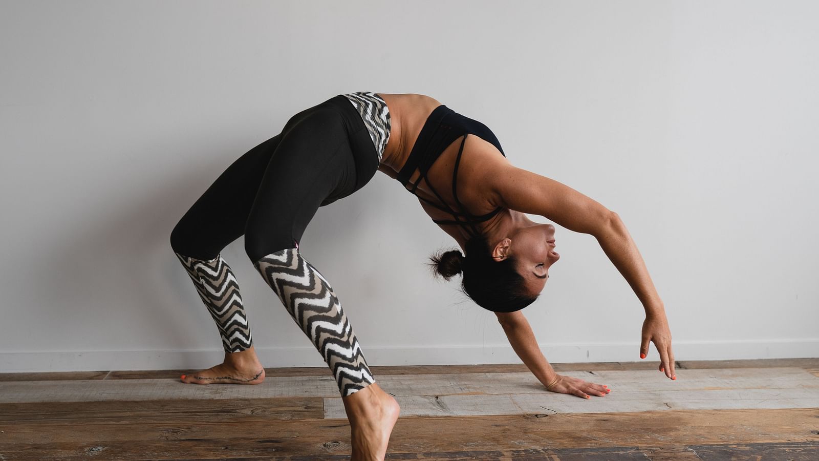 an image of a woman doing back arch stretch in front of a white wall while wearing yoya pants