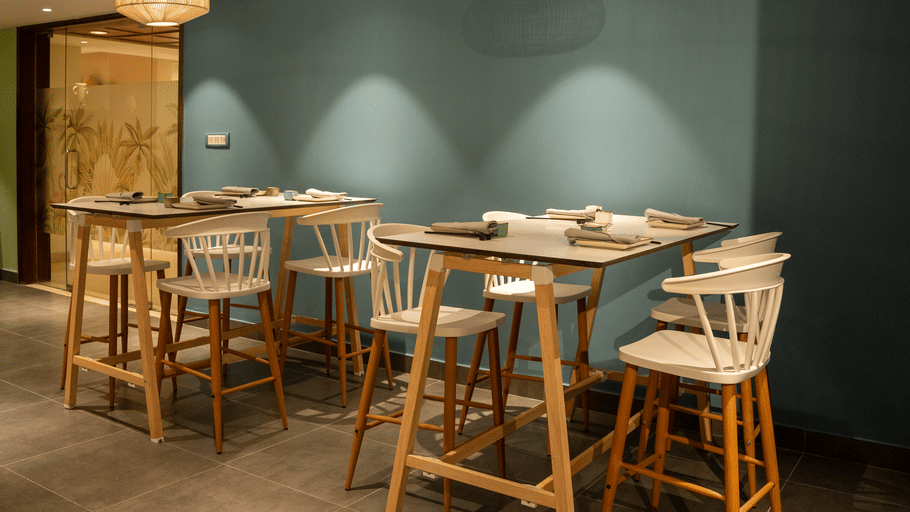 High table and bar stool seating set against a teal wall with pendant lighting at OJ Japanese Restaurant, Featherlite Evoma Hotel.