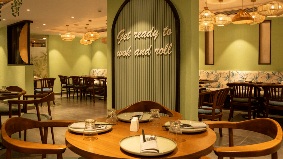 Round table seating arrangement beneath a decorative green arch wall with wooden chairs at OJ Japanese Restaurant, Featherlite Evoma Hotel.