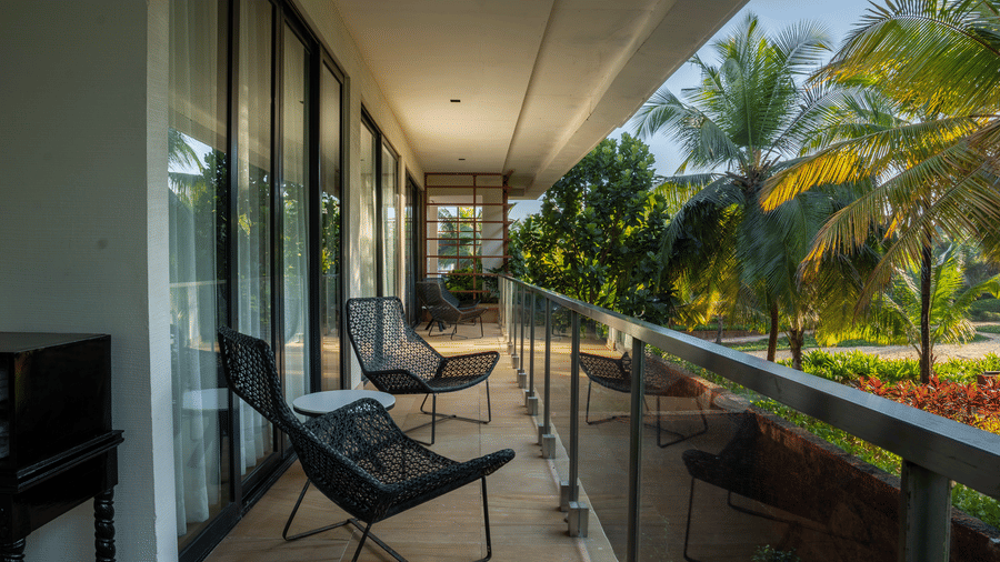 A hotel balcony with a seating area, including two black lounge chairs and a small table, overlooking a lush green landscape.