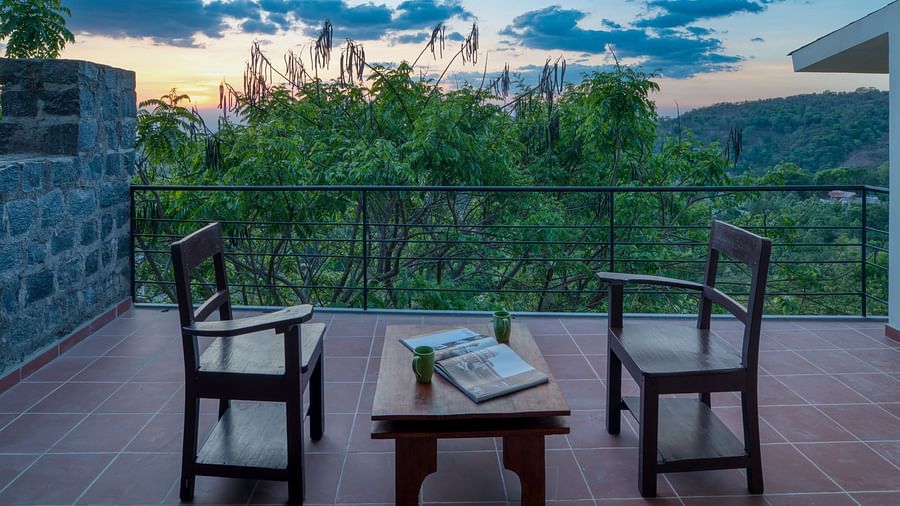 A serene balcony with two wooden chairs and a small table, overlooking a lush green landscape and a beautiful sunset.  | Mango Hill, Yercaud