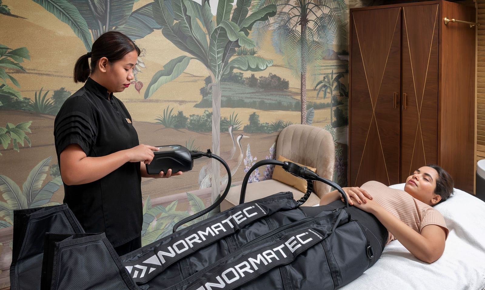 A woman administering the NORMATEC COMPRESSION THERAPY on a client at The Claridges New Delhi