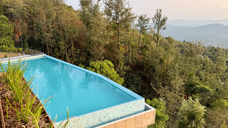 An elevated infinity swimming pool overlooking a dense green forest and hills | Kollanoor Guest House, Coorg