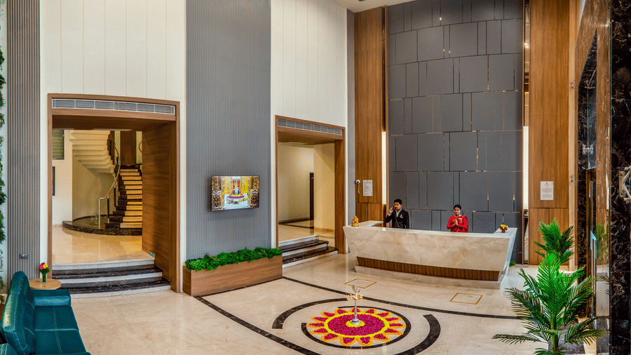 A modern hotel lobby with a marble front desk, elegant lighting, and stylish wall panels, featuring a colourful floral carpet at its centre.