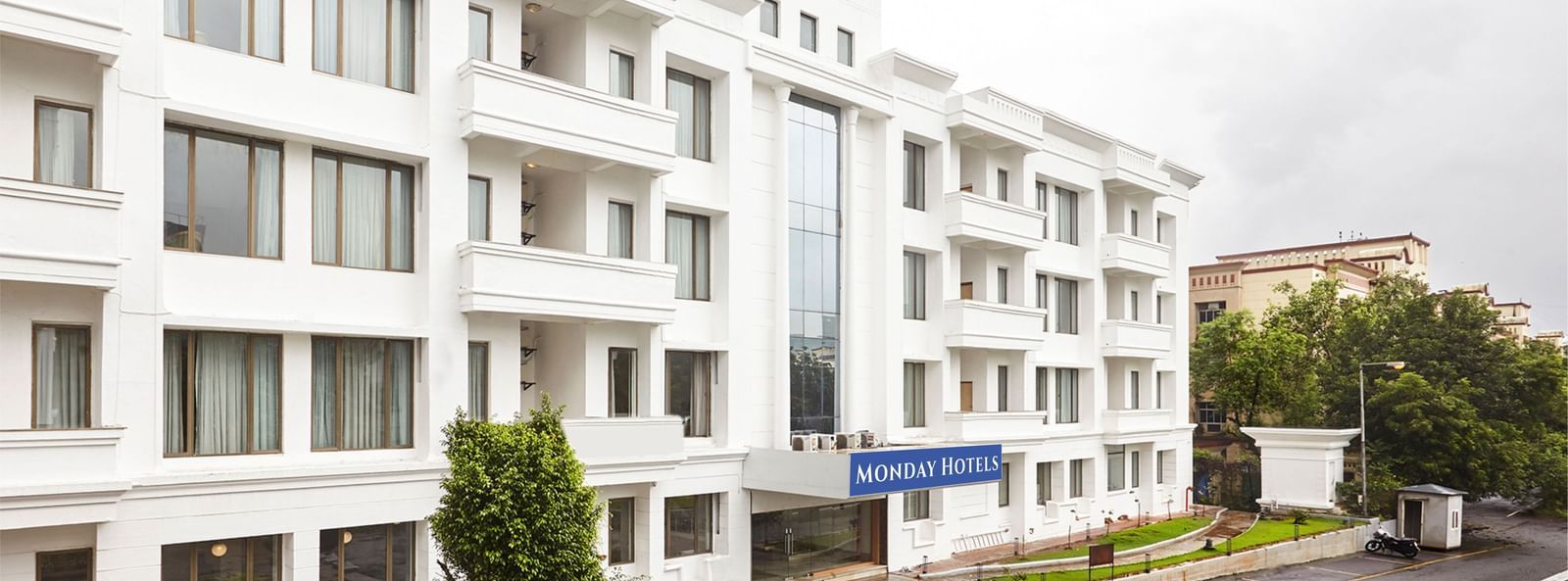 The exterior of the modern white hotel building at Monday Hotels Mahape, Navi Mumbai, with a landscaped driveway.