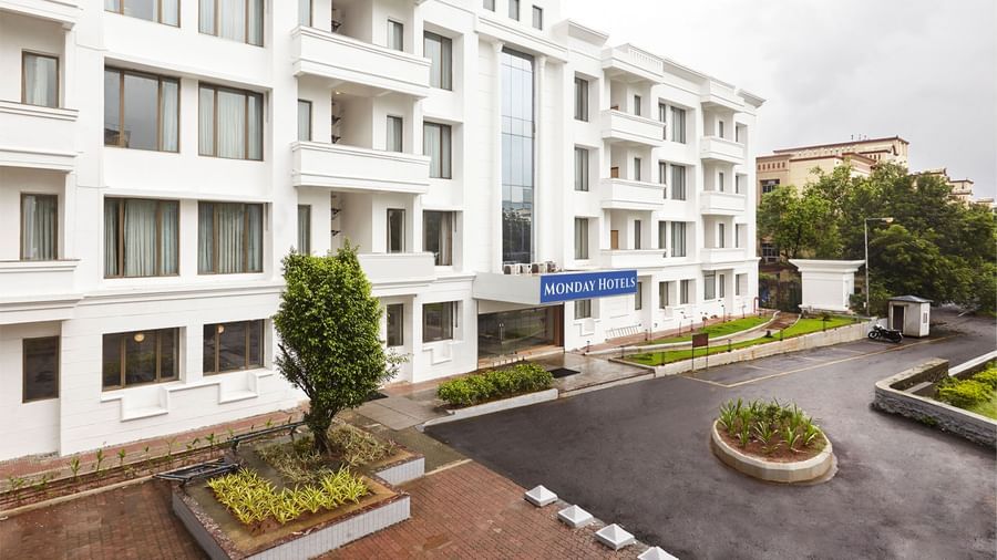 The exterior of the modern white hotel building at Monday Hotels Mahape, Navi Mumbai, with a landscaped driveway.
