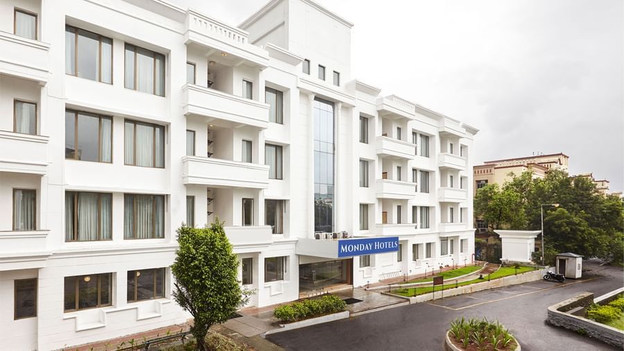 The exterior of the modern white hotel building at Monday Hotels Mahape, Navi Mumbai, with a landscaped driveway.