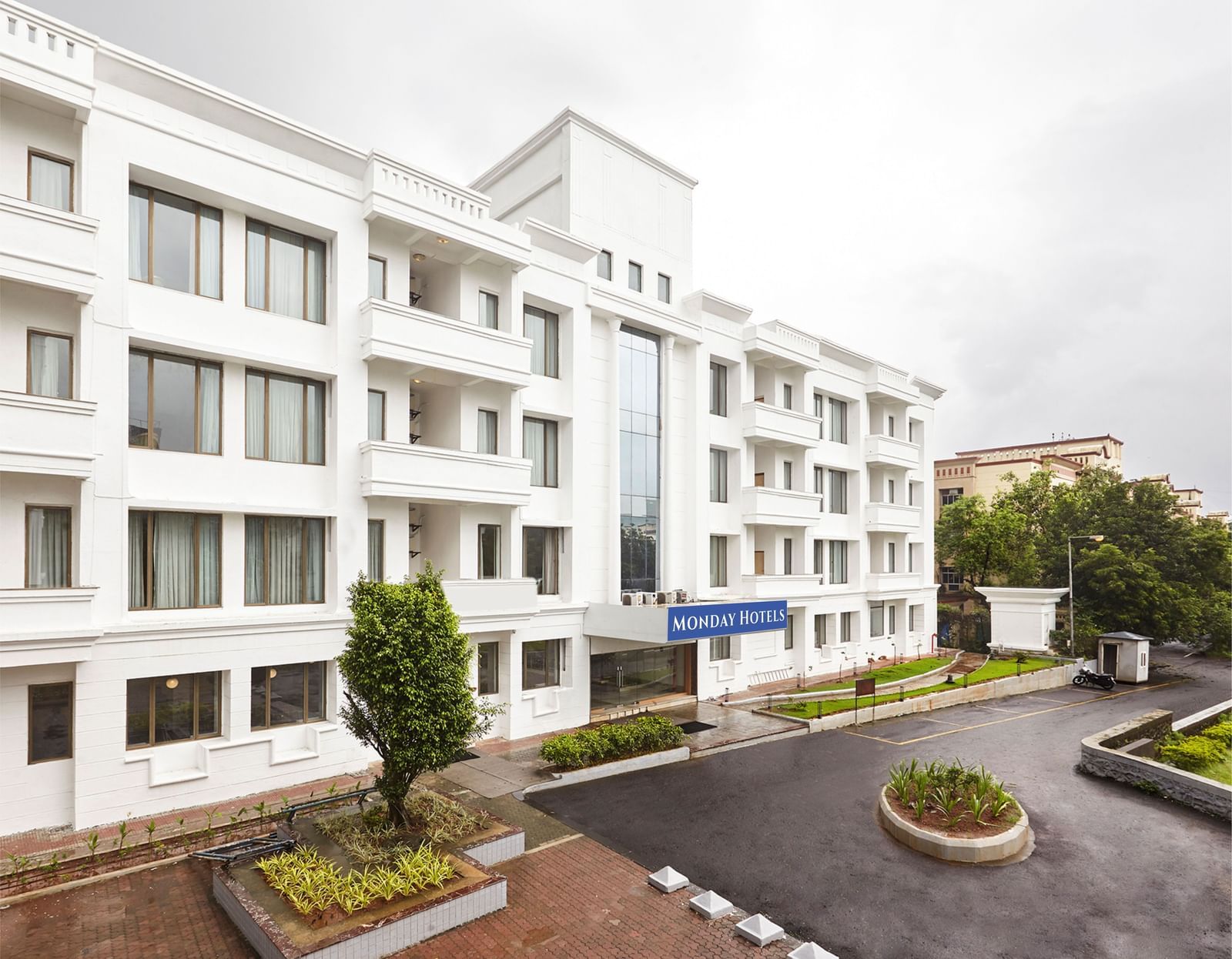 The exterior of the modern white hotel building at Monday Hotels Mahape, Navi Mumbai, with a landscaped driveway.