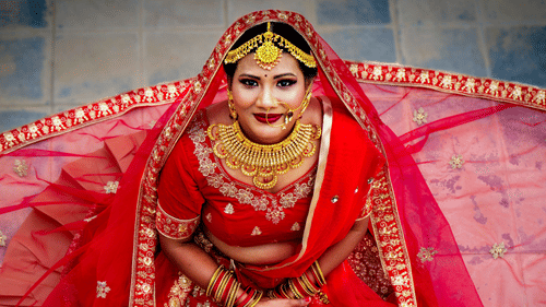A bride wearing a traditional outfit with jewelry, sitting and smiling at the camera.