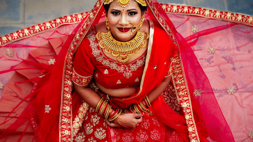 A bride wearing a traditional outfit with jewelry, sitting and smiling at the camera.