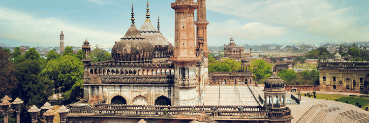 A tall, minaret-like tower with traditional architectural details and a domed structure sits under a clear sky with streaks of clouds.