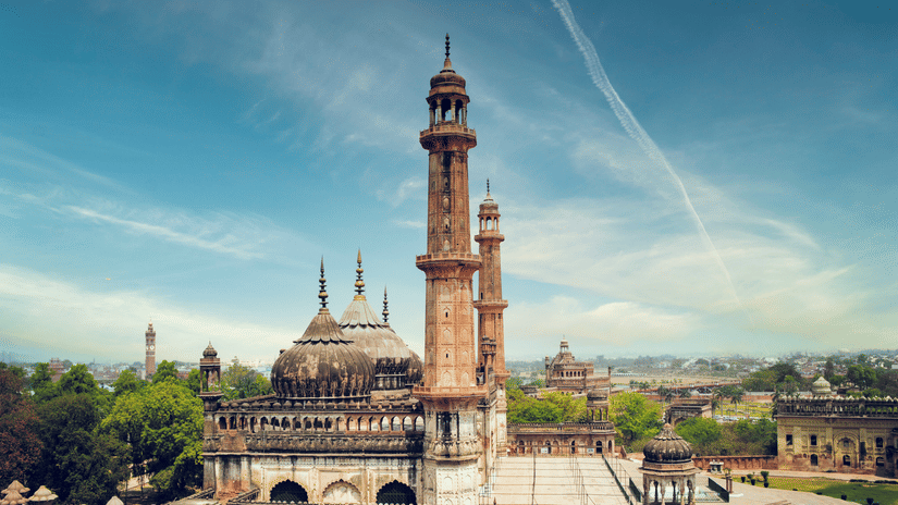 A tall, minaret-like tower with traditional architectural details and a domed structure sits under a clear sky with streaks of clouds.