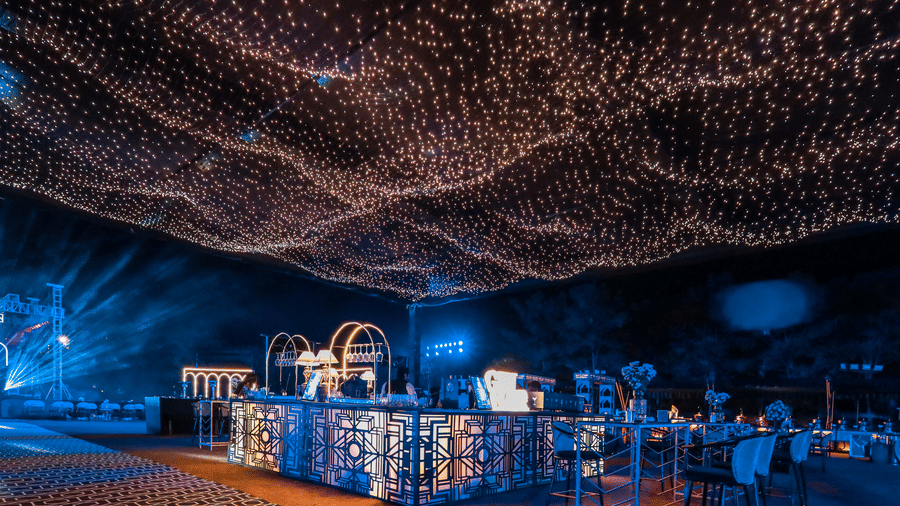Outdoor event space at Ananta Spa & Resort, Jaipur, illuminated by a dense canopy of warm fairy lights over a bar.