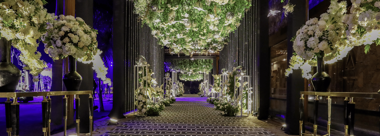 An exquisite, wide walkway at Ananta Spa & Resort, Jaipur, features a dense canopy of white flowers and lush green foliage.