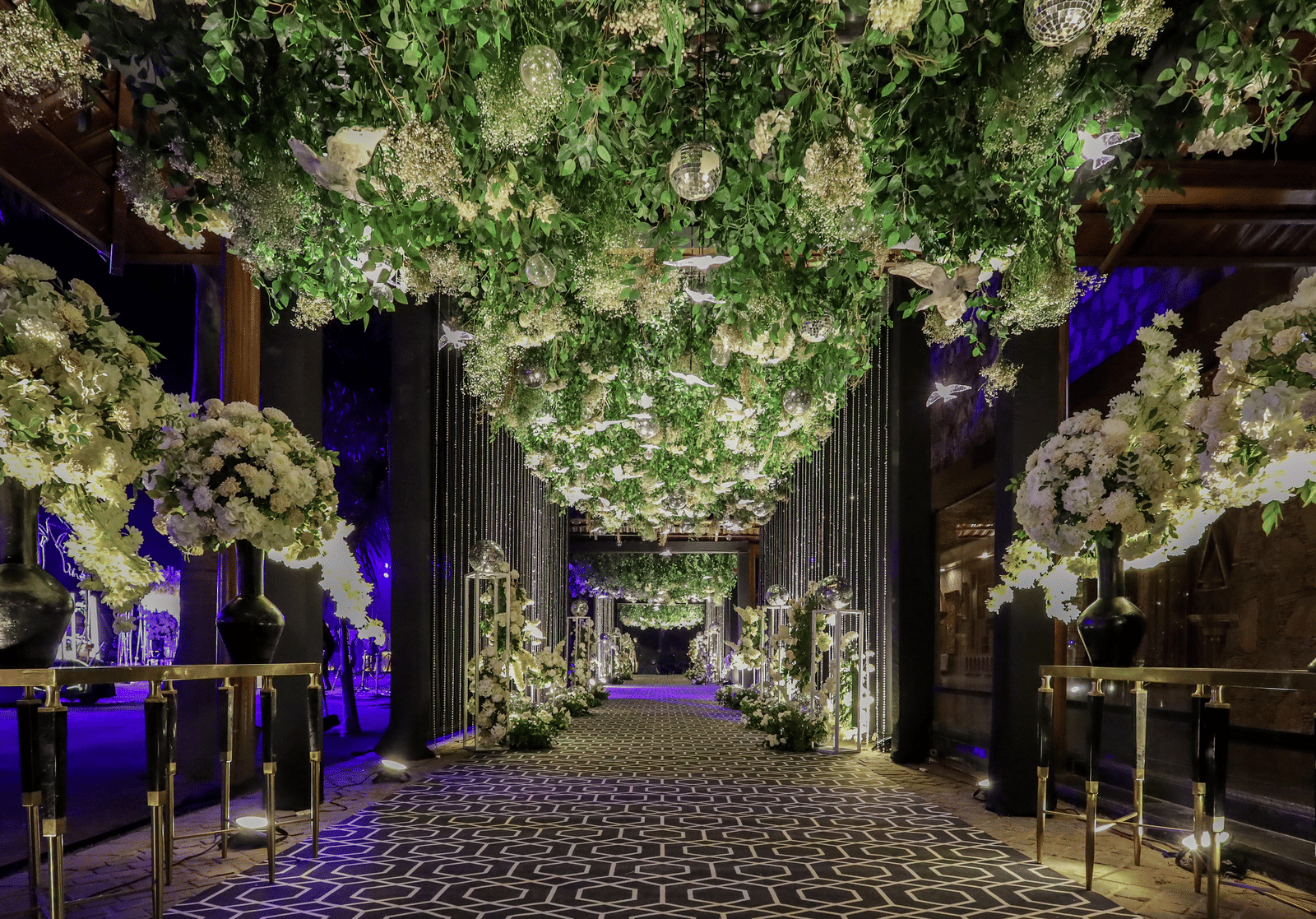 An exquisite, wide walkway at Ananta Spa & Resort, Jaipur, features a dense canopy of white flowers and lush green foliage.