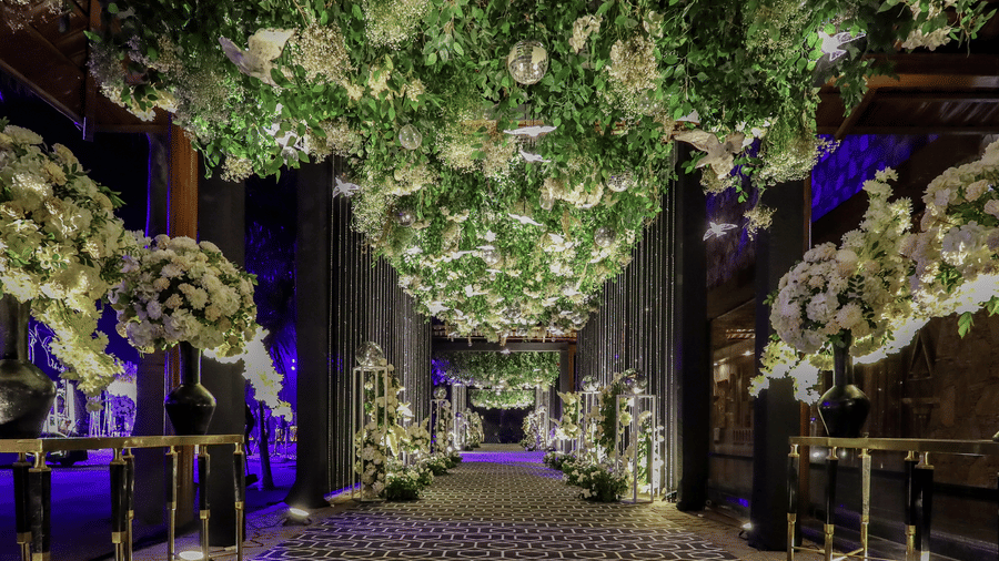 A wide walkway at Ananta Spa & Resort, Jaipur, features a dense canopy of flowers and lush green foliage.