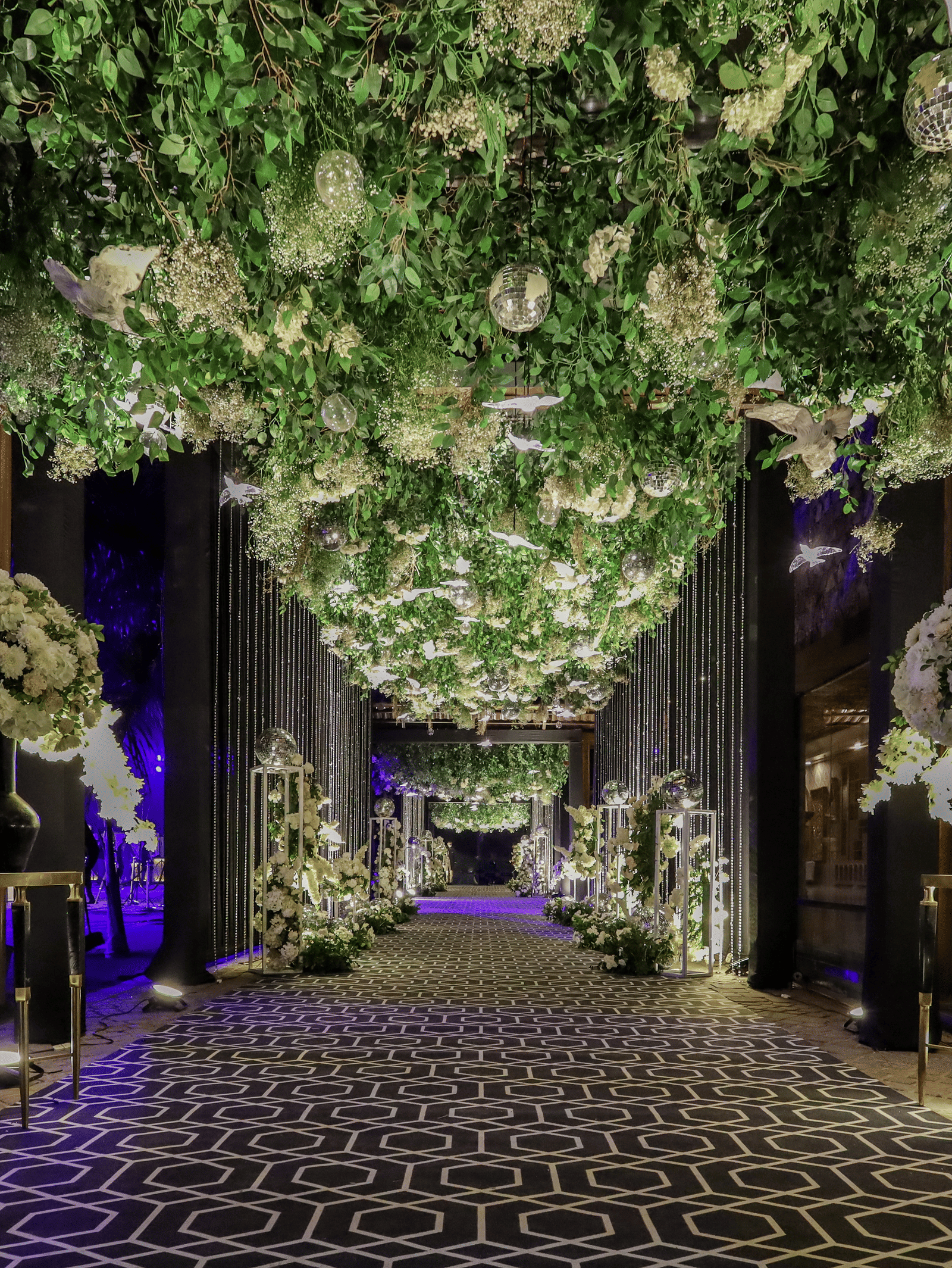 An exquisite, wide walkway at Ananta Spa & Resort, Jaipur, features a dense canopy of white flowers and lush green foliage.
