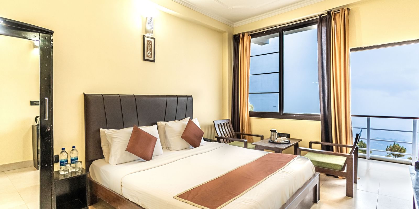 A well lit airy bedroom with a comfortable bed, table and chairs, wardrobe with a mirror,  balcony and a window overlooking the valleys.