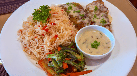 A plated meal with rice, grilled meat, sautéed vegetables, and a side of sauce served at Bhavanis Vista By Icon Hosur.