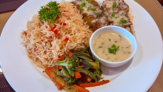 A plated meal with rice, grilled meat, sautéed vegetables, and a side of sauce served at Bhavanis Vista By Icon Hosur.