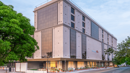  A contemporary multi-storey hotel with a beige stone facade, large glass windows, and ground-floor lighting situated on a street corner - Skkylight Lords Inn, Nanded