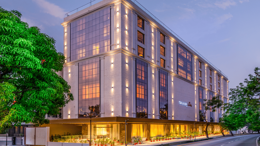The exterior of a modern multi-storey hotel at dusk, featuring a beige facade with glowing vertical lights and large glass windows along a road - Skkylight Lords Inn, Nanded