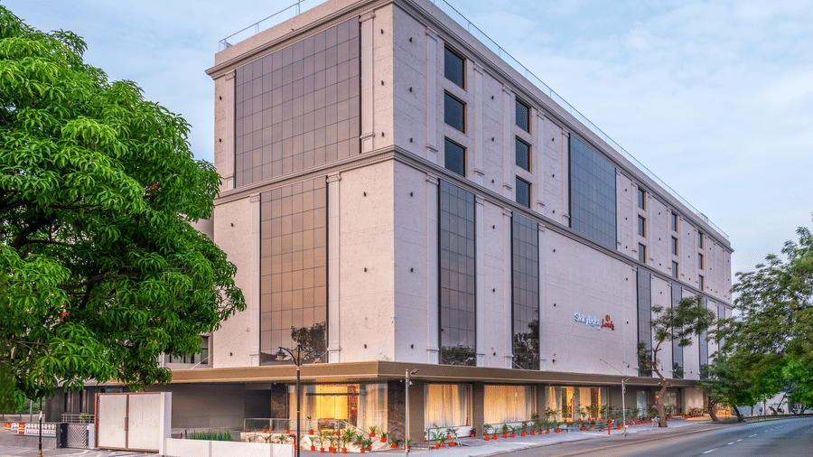  A contemporary multi-storey hotel with a beige stone facade, large glass windows, and ground-floor lighting situated on a street corner - Skkylight Lords Inn, Nanded