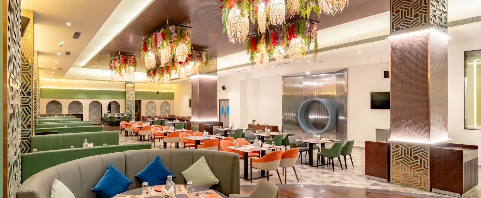 Restaurant space with orange and green seating and intricate ceiling decorations | Pravasa Hotel, Vijayapura