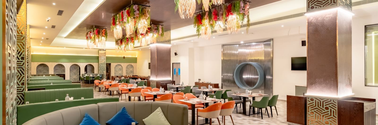 Restaurant space with orange and green seating and intricate ceiling decorations | Pravasa Hotel, Vijayapura