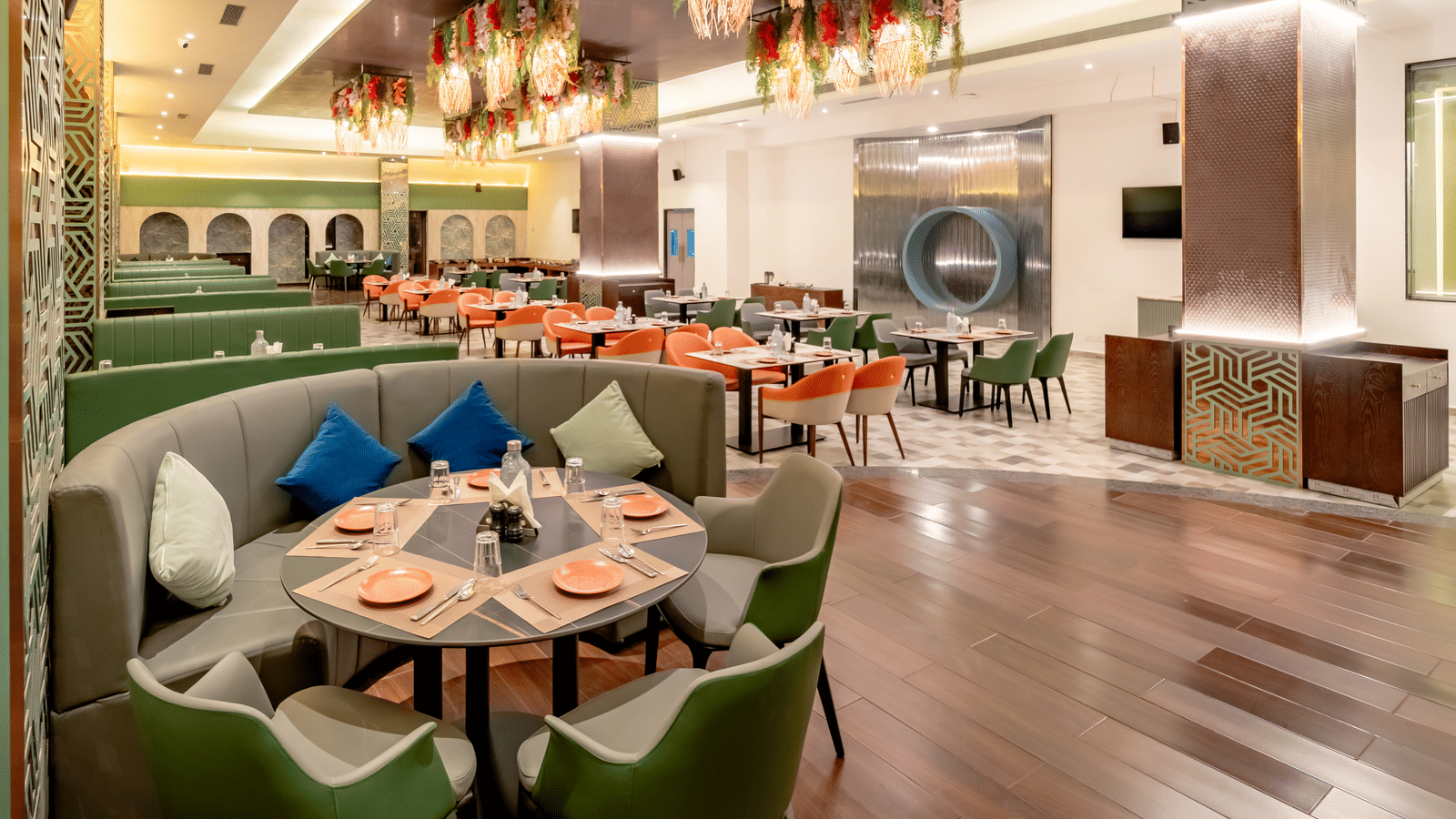 Restaurant space with orange and green seating and intricate ceiling decorations | Pravasa Hotel, Vijayapura