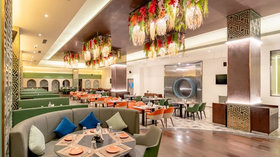 Restaurant space with orange and green seating and intricate ceiling decorations | Pravasa Hotel, Vijayapura