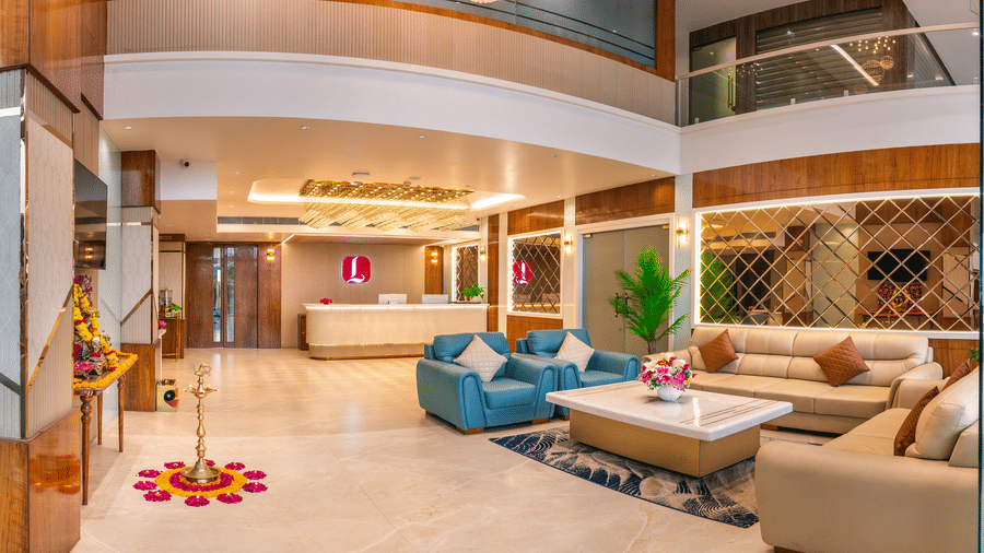 Lobby lounge area at Lords Inn Sangam, Bhopal with teal sofas, floral rangoli decorations, wooden columns, and a double-height ceiling.