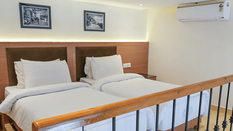 2 single beds with white bedding stand side by side behind a wooden railing at Ramada by Wyndham Mussoorie Mall Road.