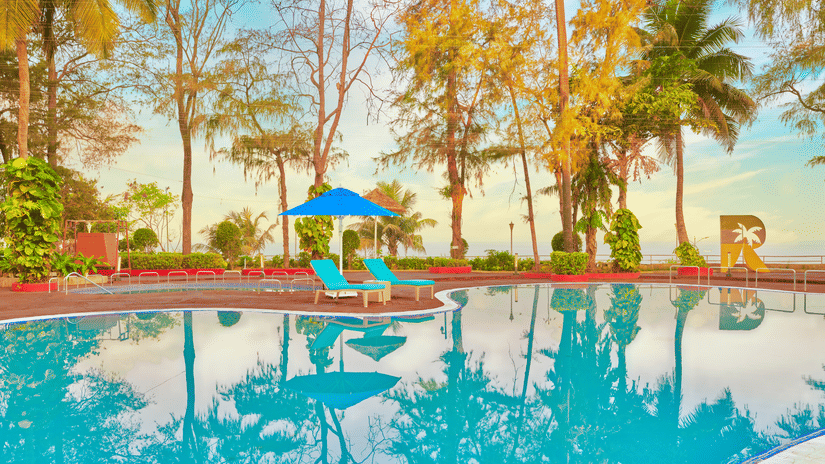 A pool surrounded by trees during the day with blue sky in the background - The Resort, Mumbai.