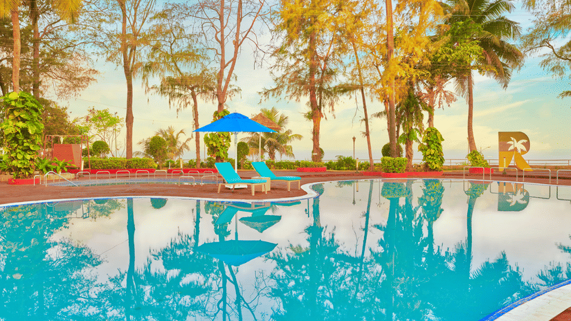 A pool surrounded by trees during the day with blue sky in the background - The Resort, Mumbai.