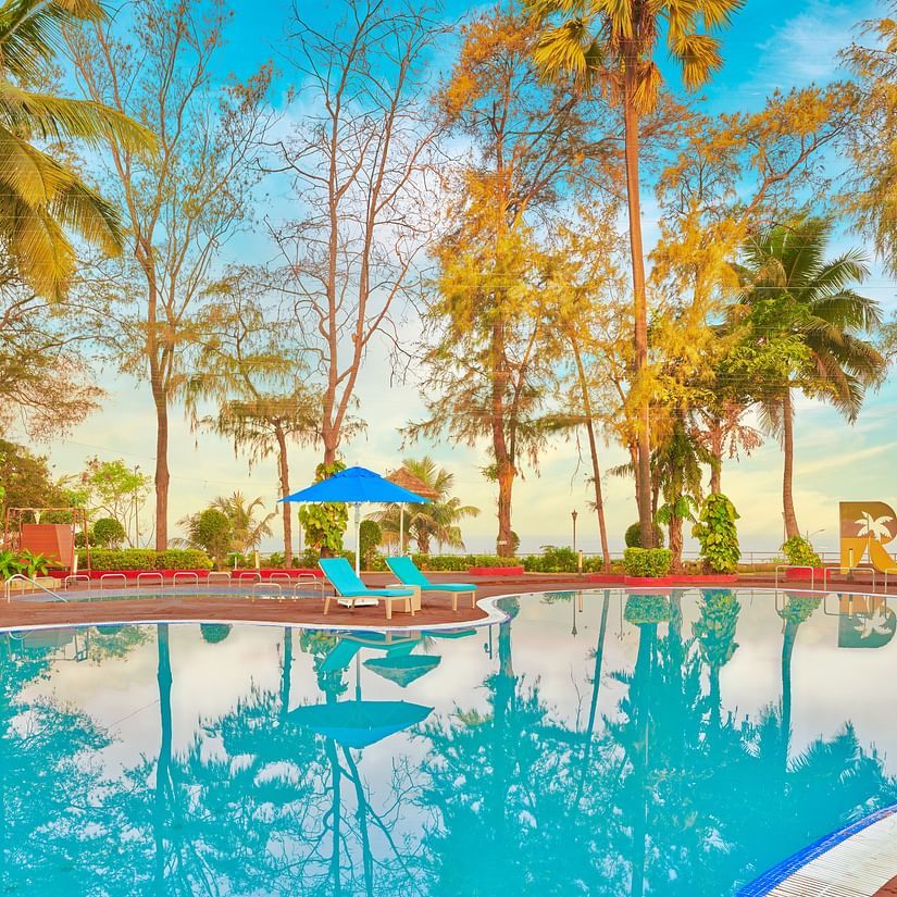 A pool surrounded by trees during the day with blue sky in the background - The Resort, Mumbai