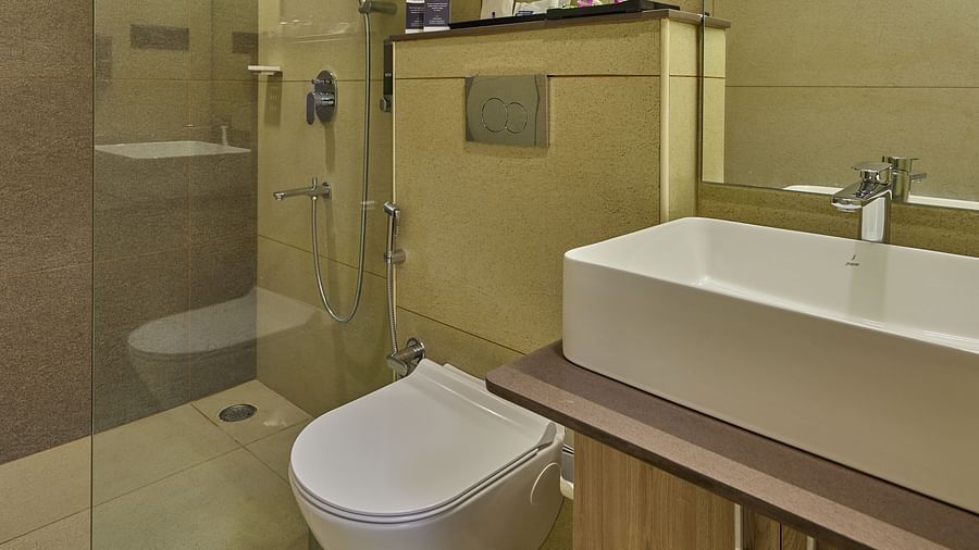 An image of a hotel bathroom with a commode, a shower cubicle and a sink placed in front of a wall mounted mirror