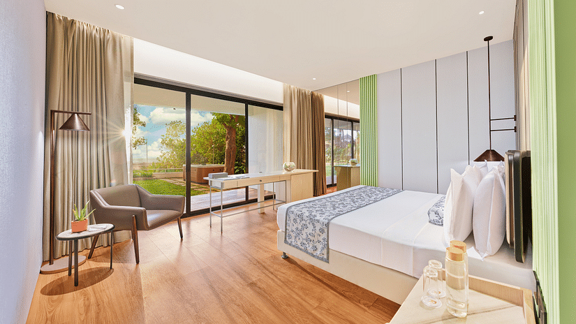 A full view of bedroom with a bed along with armchairs and a huge glass window | The Resort, Mumbai