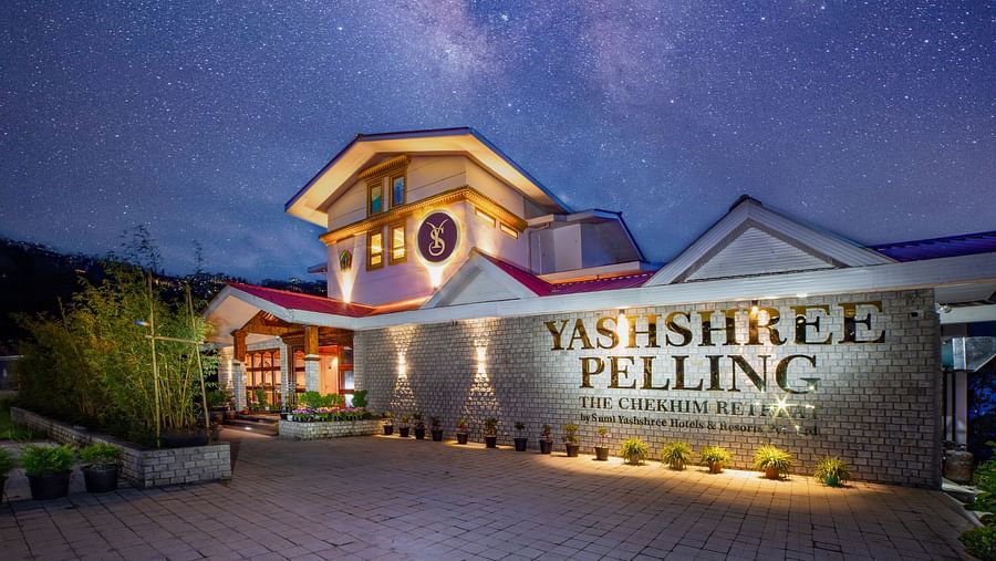 Nighttime view of Yashshree Pelling, a beautifully lit hotel with a stone façade and red-roofed building, under a stunning starry sky with the Milky Way visible.