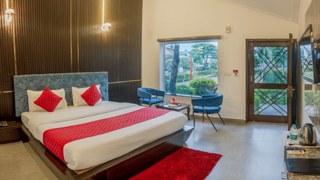 Full view of the bedroom of the Deluxe Cottage featuring a double bed with a red bed runner and a re carpet placed on the floor at Corbett Holiday Forest Resort, Ramnagar.