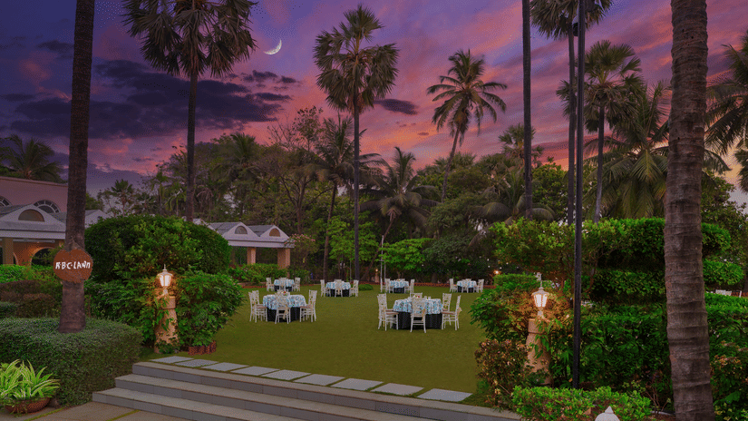 An overview of the entrance to the RBC lawn with round table seating arrangements at The Resort, Mumbai, during twilight hour - The Best Wedding Destination in Mumbai.