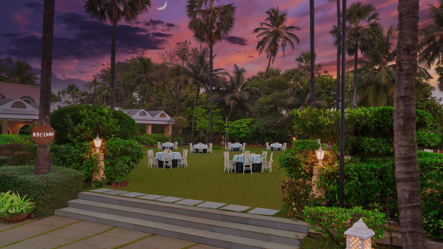 An overview of the entrance to the RBC lawn with round table seating arrangements at The Resort, Mumbai, during twilight hour - The Best Wedding Destination in Mumbai.