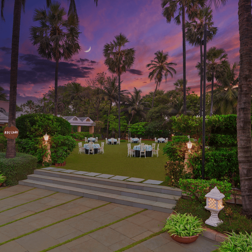 An overview of the entrance to the RBC lawn with round table seating arrangements at The Resort, Mumbai, during twilight hour - The Best Wedding Destination in Mumbai.