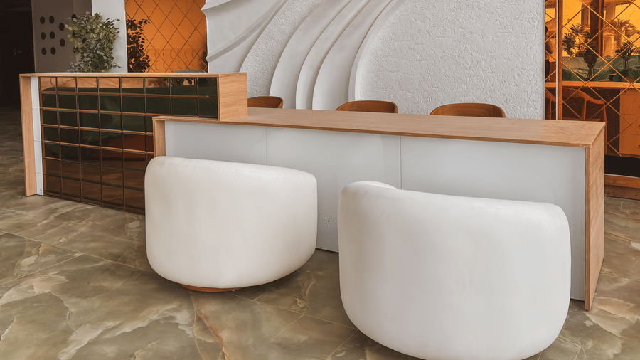 A reception desk with 2 white chairs stands in front of a large white wall featuring a 3D wave pattern at Avanya Resorts N Retreat.