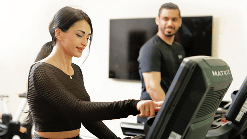 a couple inside the gymnasium on a treadmill while the man looks at the woman