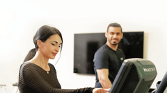 a couple inside the gymnasium on a treadmill while the man looks at the woman