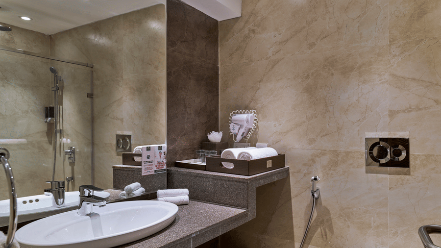 The bathroom of Premium King Room at Swosti Premium, Bhubaneswar, featuring a sink, toileteries, a toilet, and a mirror.