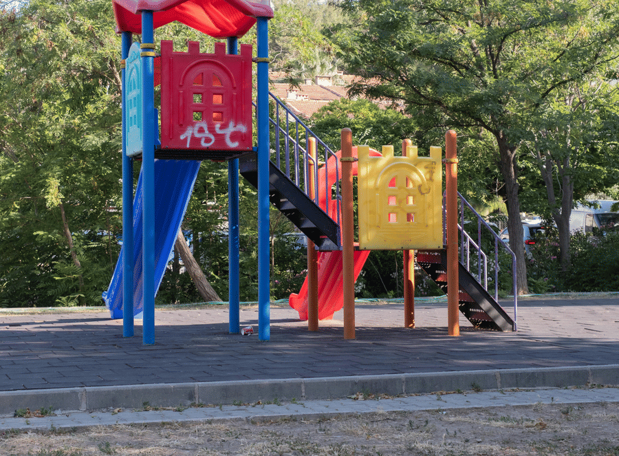 A colourful children's playground set with a blue slide and a red roof located in a park setting.