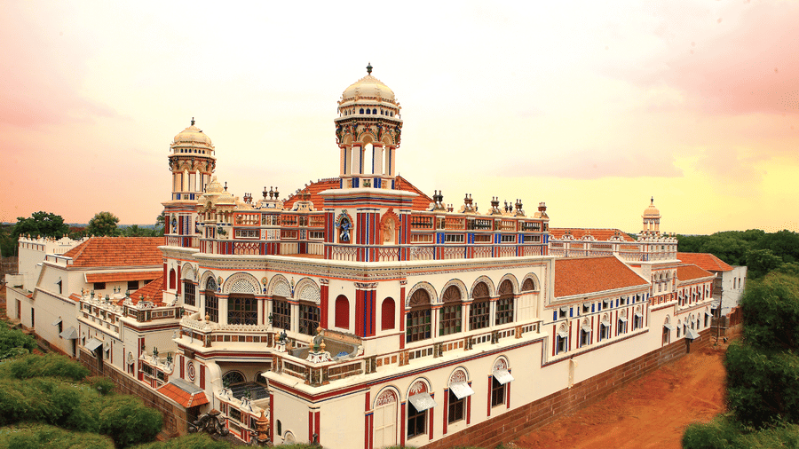 Facade view of Chidambara Vilas - A Luxury Chettinad Heritage Resort, surrounded by greenery and pink skies. 