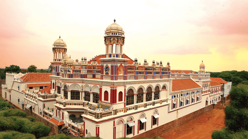 Facade view of Chidambara Vilas - A Luxury Chettinad Heritage Resort, surrounded by greenery and pink skies. 